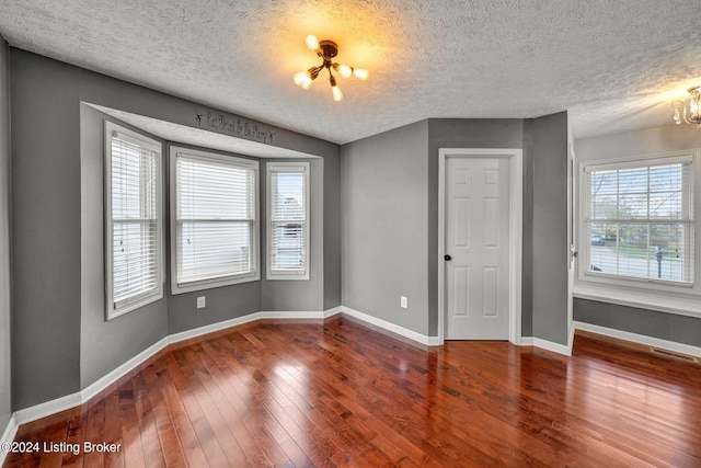 empty room featuring hardwood / wood-style floors, a textured ceiling, a wealth of natural light, and a chandelier