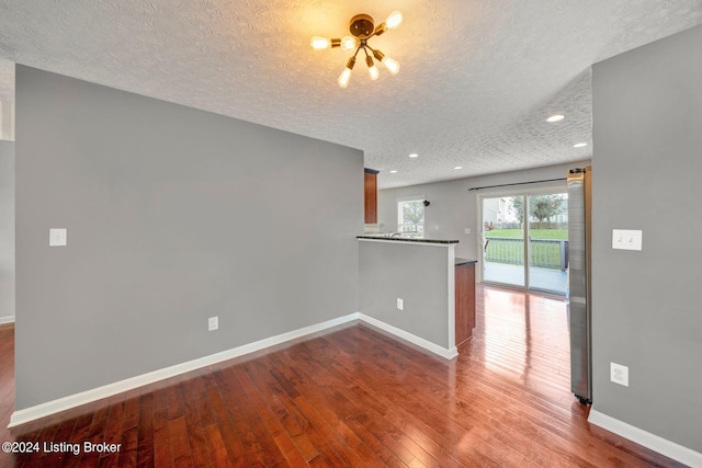 empty room featuring wood-type flooring, a textured ceiling, and an inviting chandelier