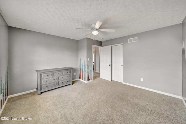 unfurnished bedroom with ceiling fan, light colored carpet, a textured ceiling, and a closet