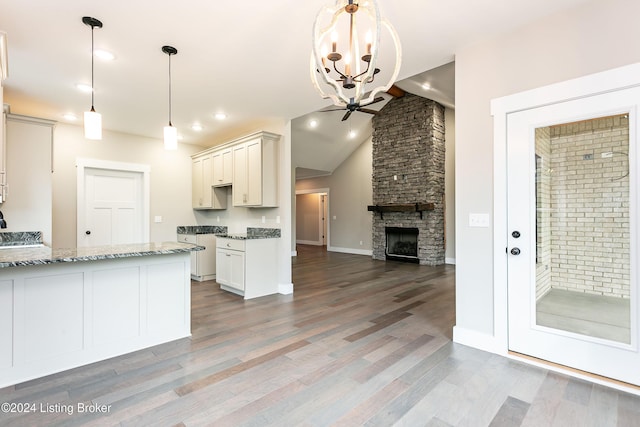 kitchen featuring light stone counters, wood-type flooring, pendant lighting, white cabinetry, and a stone fireplace