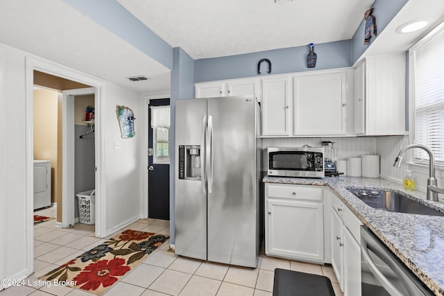 kitchen featuring sink, light tile patterned floors, washer / dryer, white cabinets, and appliances with stainless steel finishes