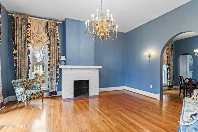 living room featuring hardwood / wood-style floors, a notable chandelier, and a brick fireplace