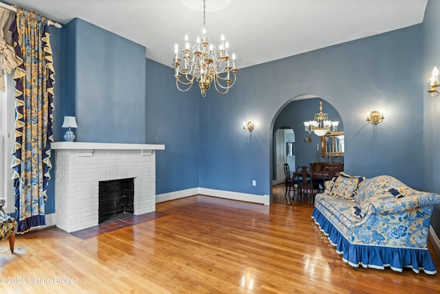 living room featuring hardwood / wood-style floors, an inviting chandelier, and a brick fireplace