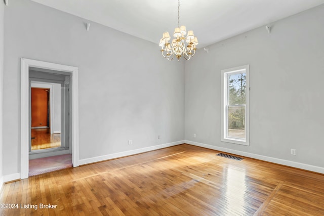 empty room featuring wood-type flooring and a chandelier