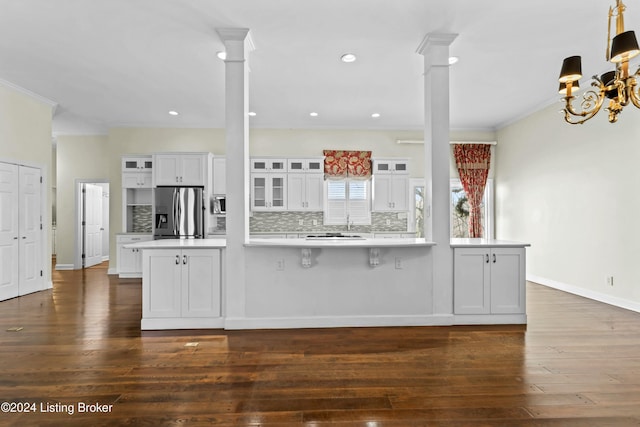 kitchen with ornate columns, tasteful backsplash, kitchen peninsula, white cabinets, and appliances with stainless steel finishes