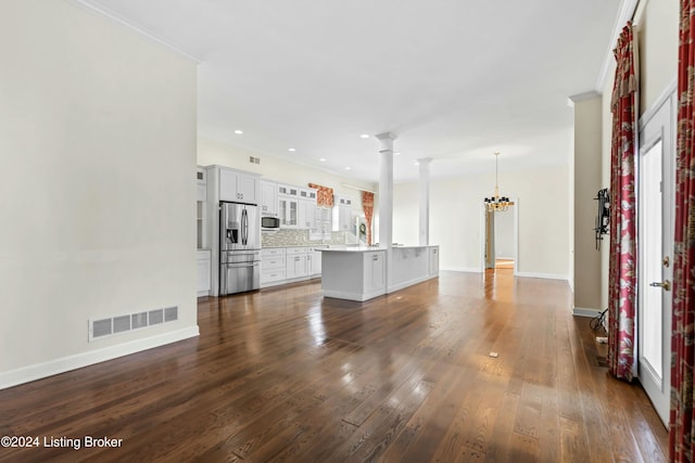 unfurnished living room with sink, crown molding, dark hardwood / wood-style floors, a notable chandelier, and decorative columns