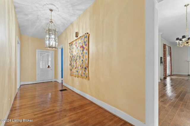 corridor featuring wood-type flooring and an inviting chandelier