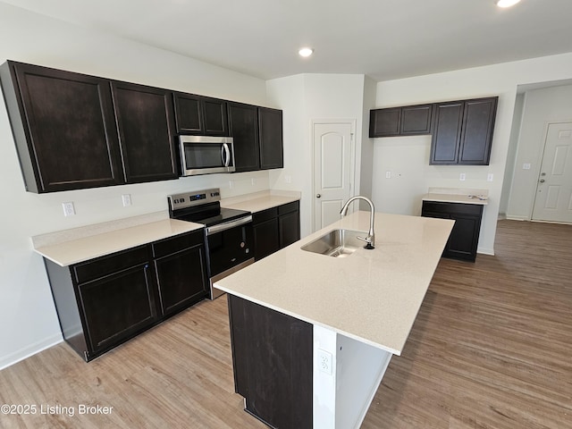 kitchen featuring a kitchen island with sink, appliances with stainless steel finishes, a sink, and light wood-style flooring