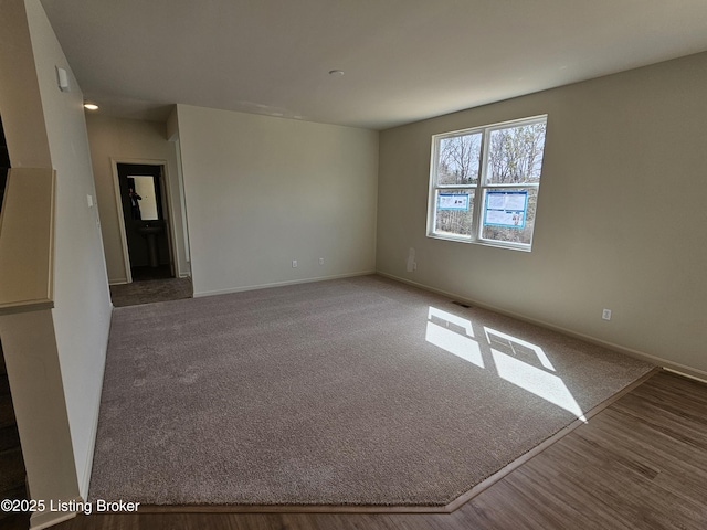 carpeted empty room featuring baseboards, visible vents, and wood finished floors