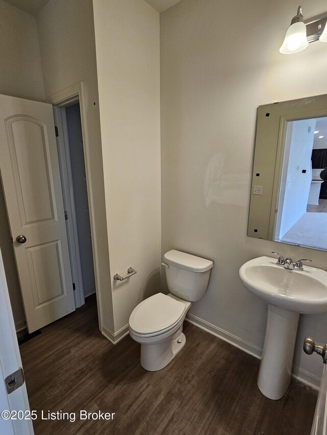 half bath with a sink, wood finished floors, toilet, and baseboards