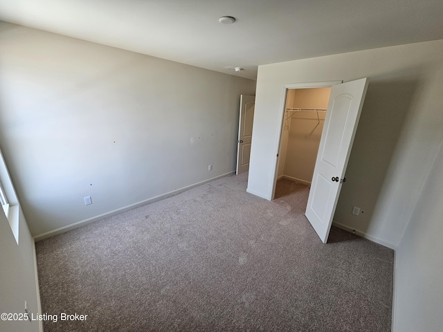 unfurnished bedroom with carpet flooring, a spacious closet, and baseboards