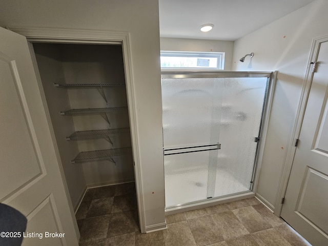 bathroom with a shower stall, a walk in closet, and baseboards