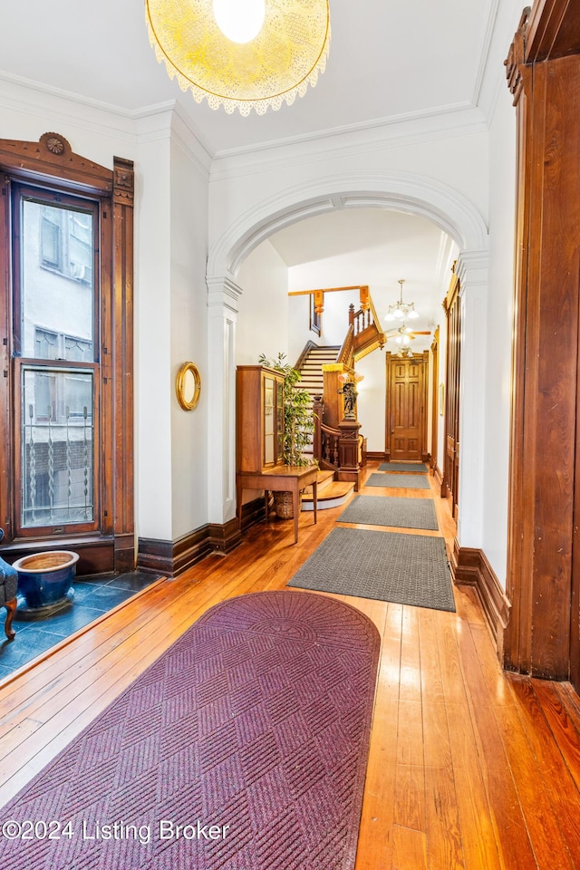 hallway featuring wood-type flooring, crown molding, and ornate columns