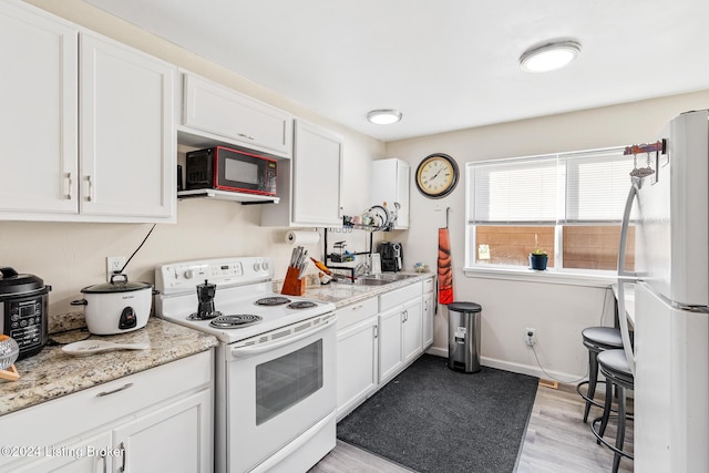 kitchen with white cabinets, light wood-type flooring, white appliances, and light stone counters