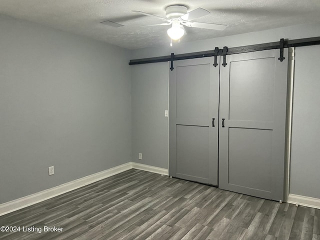 unfurnished bedroom with ceiling fan, dark hardwood / wood-style floors, a barn door, and a textured ceiling