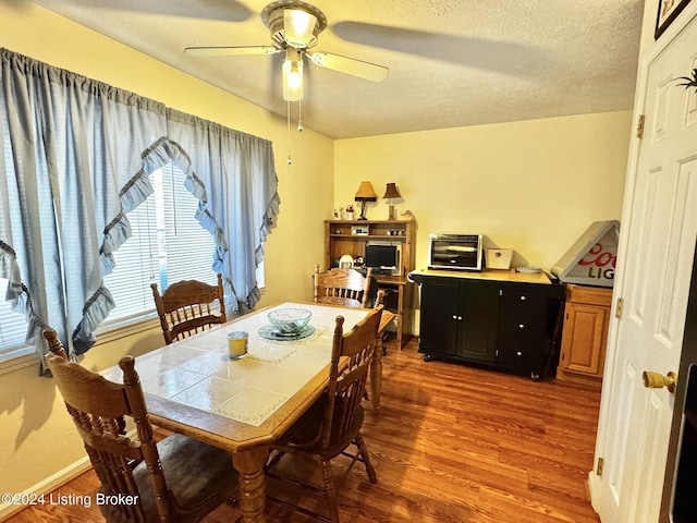 dining space with hardwood / wood-style flooring, ceiling fan, and a textured ceiling