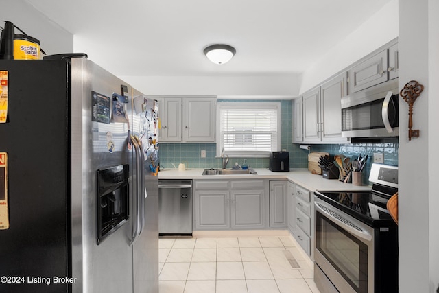 kitchen with backsplash, stainless steel appliances, sink, light tile patterned floors, and gray cabinets