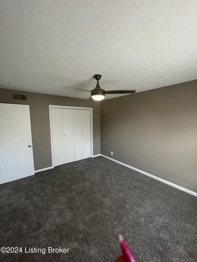 unfurnished bedroom featuring ceiling fan, dark carpet, a textured ceiling, and a closet