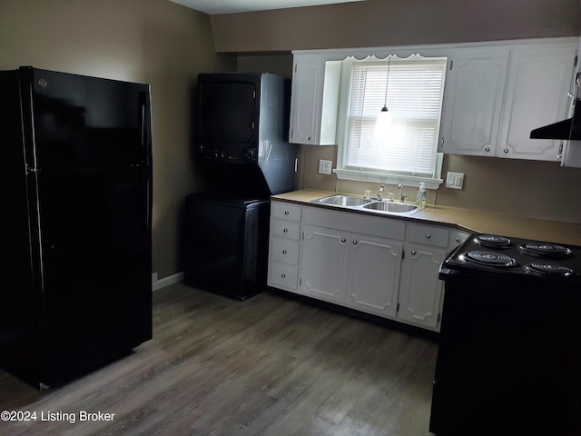 kitchen featuring stove, black refrigerator, sink, stacked washing maching and dryer, and white cabinetry