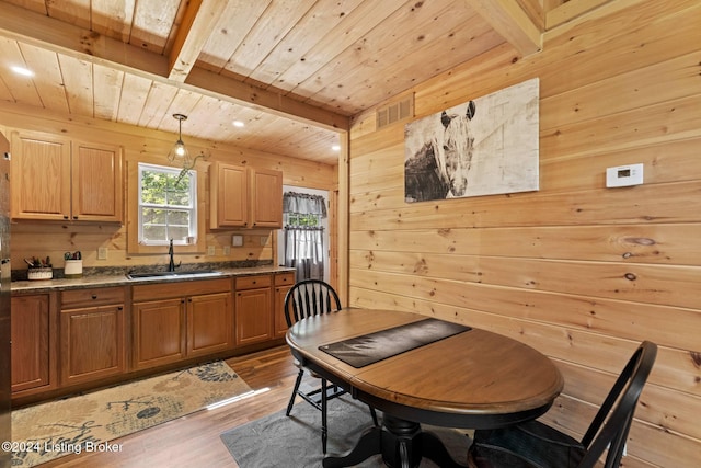 dining area featuring hardwood / wood-style flooring, wood walls, sink, and beamed ceiling