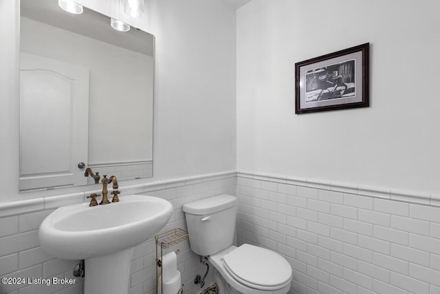 bathroom with sink, toilet, and tile walls