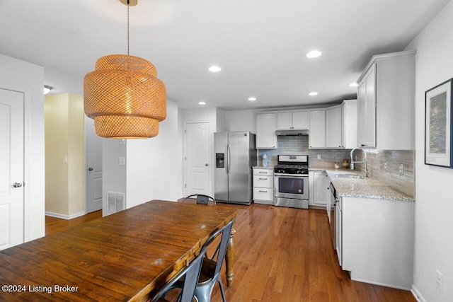 kitchen featuring white cabinets, sink, hanging light fixtures, light stone counters, and stainless steel appliances