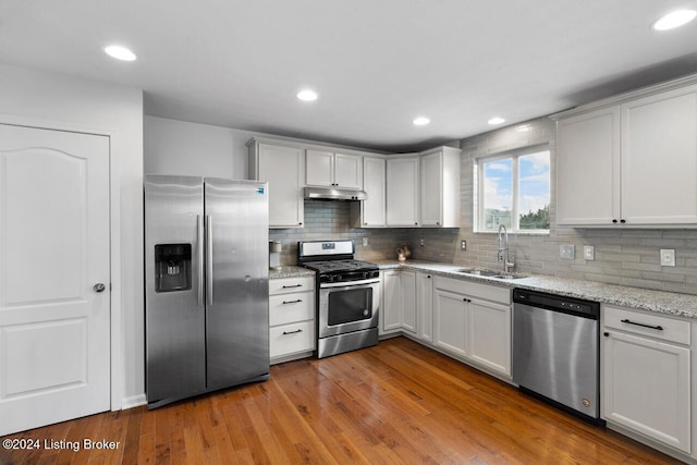 kitchen with white cabinets, sink, light hardwood / wood-style floors, light stone counters, and stainless steel appliances