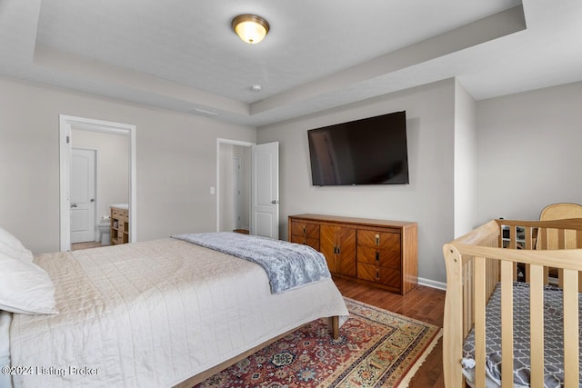 bedroom with a raised ceiling, ensuite bathroom, and hardwood / wood-style flooring