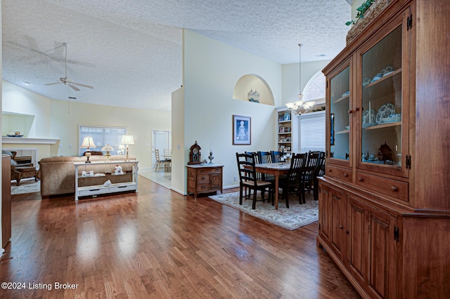 dining area with ceiling fan with notable chandelier, dark hardwood / wood-style flooring, a textured ceiling, and high vaulted ceiling