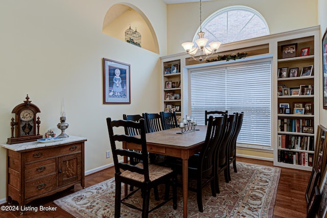 dining space with built in shelves, dark hardwood / wood-style flooring, a towering ceiling, and an inviting chandelier