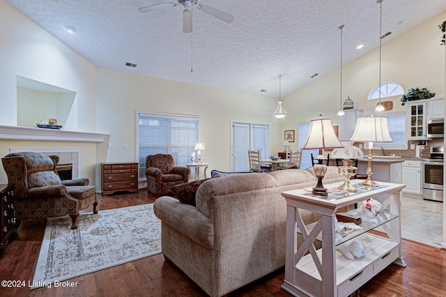 living room featuring a textured ceiling, ceiling fan, dark wood-type flooring, sink, and high vaulted ceiling