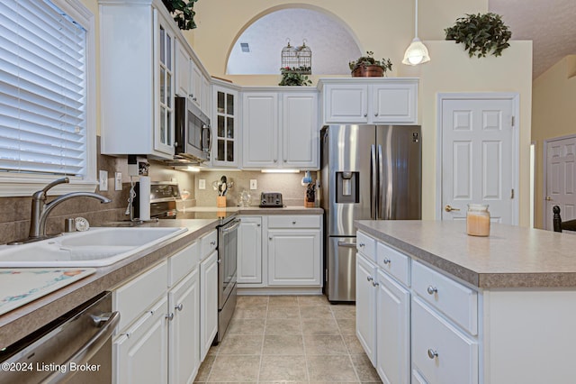 kitchen with appliances with stainless steel finishes, sink, pendant lighting, white cabinets, and a kitchen island