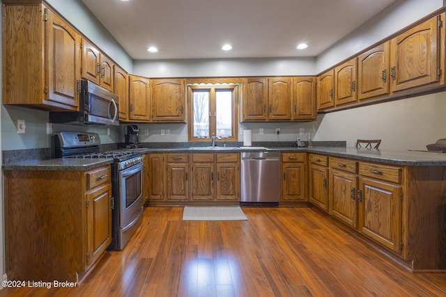 kitchen with sink, dark stone countertops, stainless steel appliances, dark hardwood / wood-style floors, and kitchen peninsula