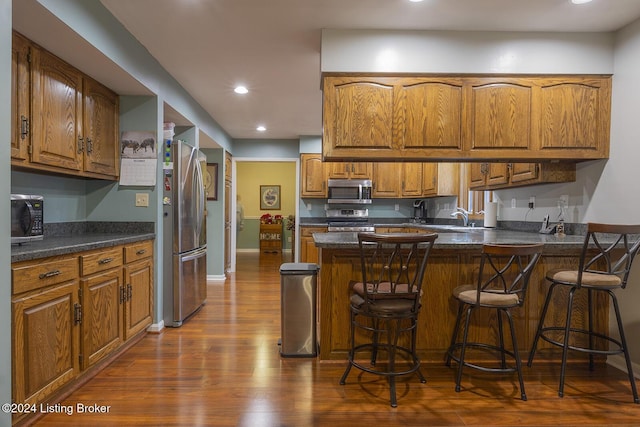 kitchen featuring sink, a breakfast bar area, stainless steel appliances, dark hardwood / wood-style floors, and kitchen peninsula