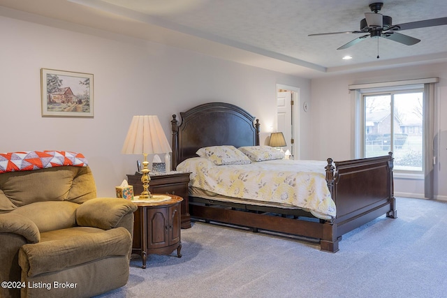 bedroom featuring light colored carpet, a raised ceiling, and ceiling fan