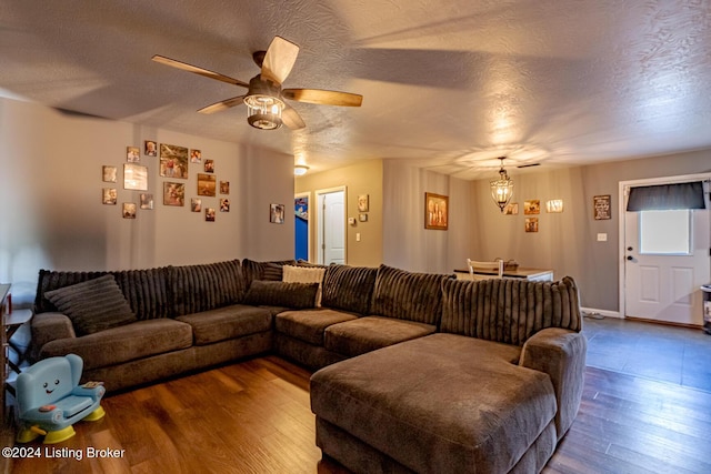 living room with ceiling fan with notable chandelier, wood-type flooring, and a textured ceiling