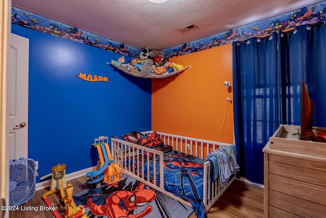 bedroom featuring a textured ceiling, a crib, and hardwood / wood-style flooring