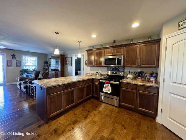 kitchen with kitchen peninsula, appliances with stainless steel finishes, dark hardwood / wood-style flooring, and decorative light fixtures