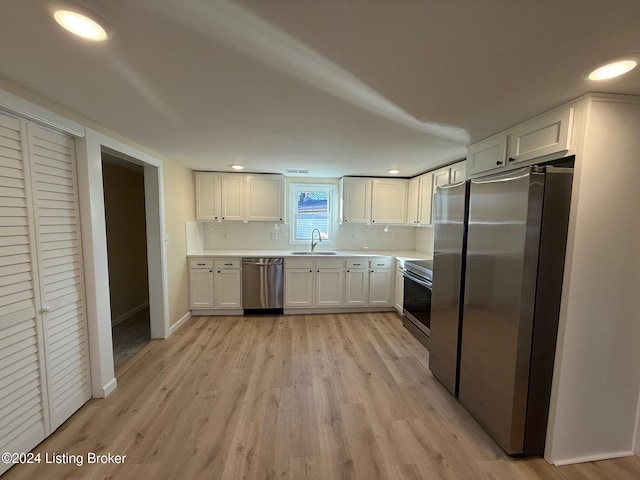 kitchen featuring light wood-type flooring, backsplash, stainless steel appliances, sink, and white cabinets