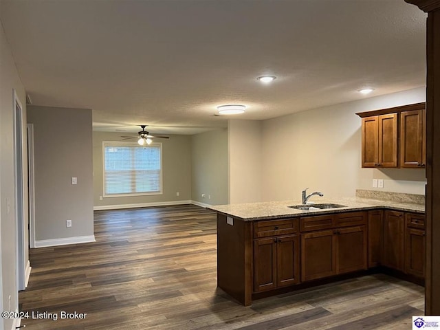 kitchen with ceiling fan, sink, light stone counters, dark hardwood / wood-style flooring, and kitchen peninsula