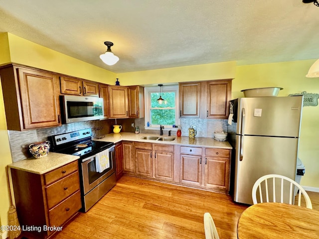 kitchen featuring sink, hanging light fixtures, stainless steel appliances, backsplash, and light hardwood / wood-style floors