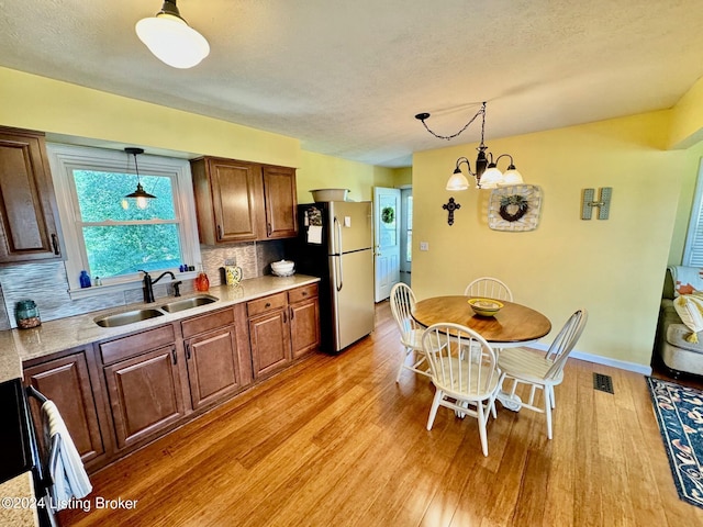 kitchen featuring stainless steel fridge, backsplash, sink, light hardwood / wood-style flooring, and a notable chandelier