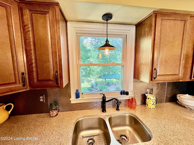 kitchen featuring light stone counters, sink, and hanging light fixtures