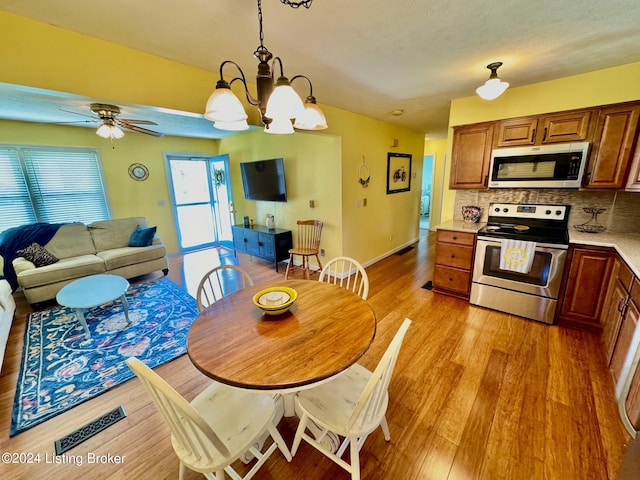 kitchen featuring ceiling fan with notable chandelier, light wood-type flooring, tasteful backsplash, decorative light fixtures, and stainless steel appliances