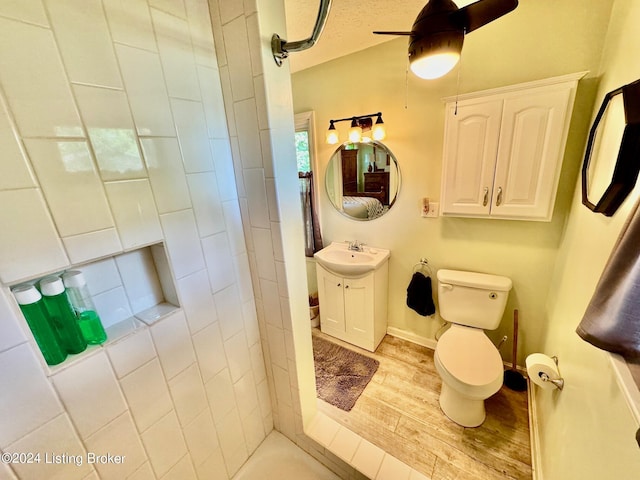 bathroom with a tile shower, vanity, ceiling fan, hardwood / wood-style flooring, and toilet