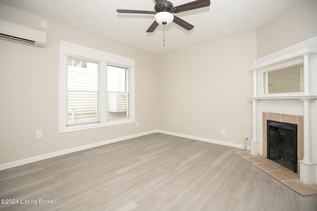 unfurnished living room featuring a tiled fireplace, a textured ceiling, wood finished floors, a wall mounted air conditioner, and baseboards