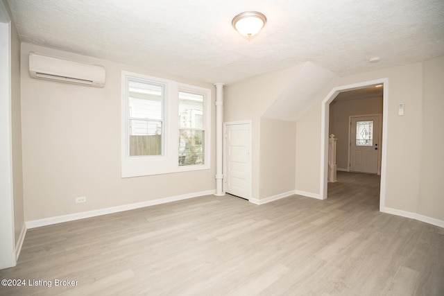 bonus room with light wood finished floors, a textured ceiling, and a wall mounted air conditioner