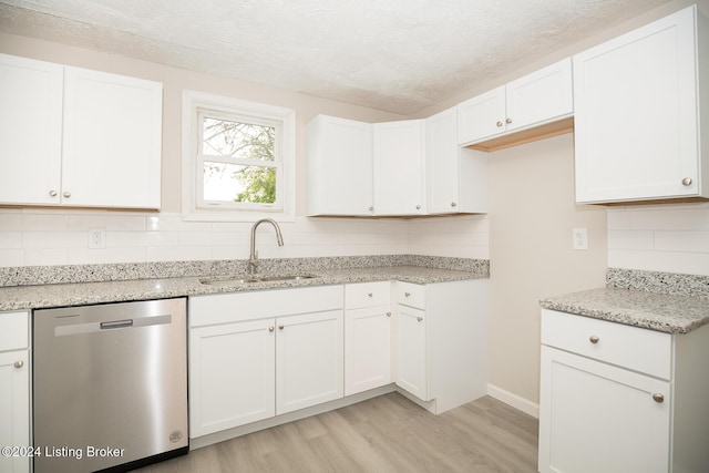 kitchen with white cabinetry, a sink, stainless steel dishwasher, and light stone countertops