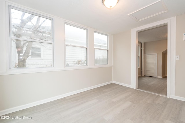 empty room featuring light wood finished floors, attic access, and baseboards