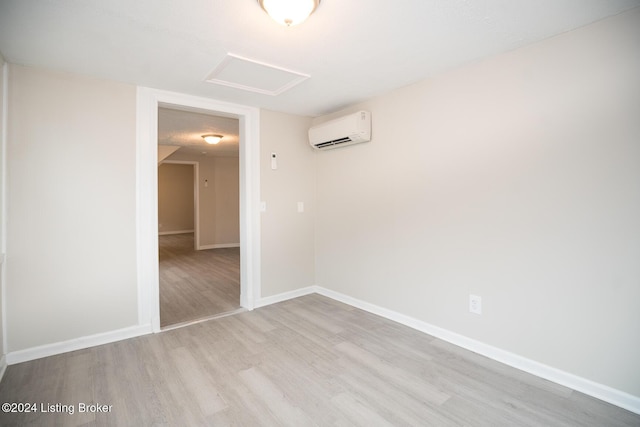 empty room featuring attic access, light wood-type flooring, a wall mounted air conditioner, and baseboards